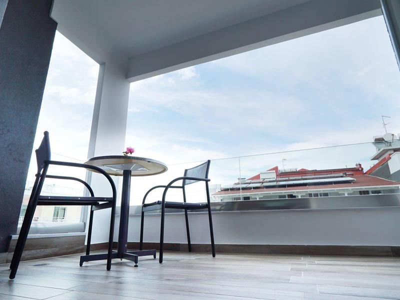 Balkon met twee stoelen en tafel met uitzicht op daken bij bewolkte lucht.