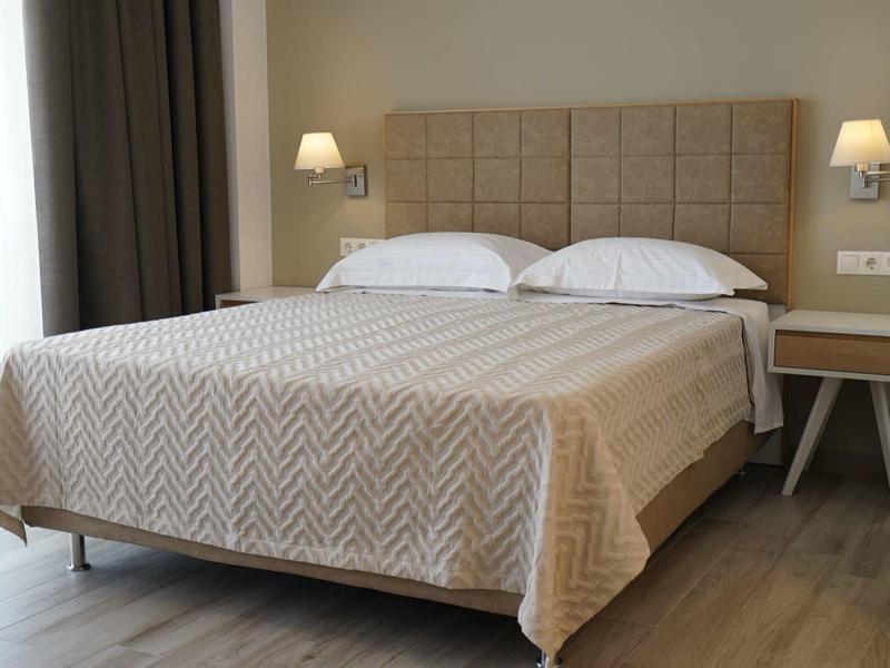 Moderne hotelkamer met tweepersoonsbed, beige bedsprei en wandlampen naast het bed.