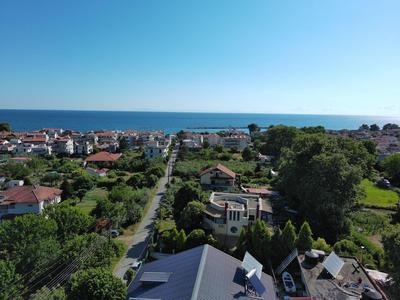 Vista de una ciudad costera con casas, árboles y el mar al fondo.