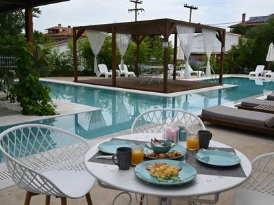 Une table dressée avec repas près d'une piscine d'hôtel avec chaises longues et pavillon.