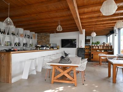 Café moderne et lumineuse avec plafond en bois, chaises blanches et grandes fenêtres.