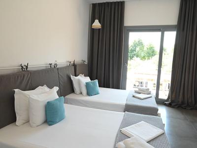 Habitación de hotel moderna con dos camas, cojines azules y balcón con vista.