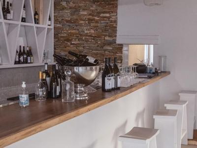 Espace bar moderne avec comptoir en bois, tabourets blancs et mur en pierre décorative.