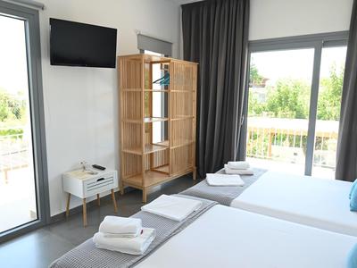 Habitación de hotel moderna con dos camas, vista al balcón y televisor en la pared.