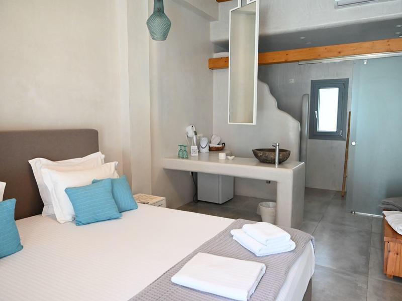 Habitación de hotel moderna con cama doble, almohadas, toallas y espejo sobre un lavabo.