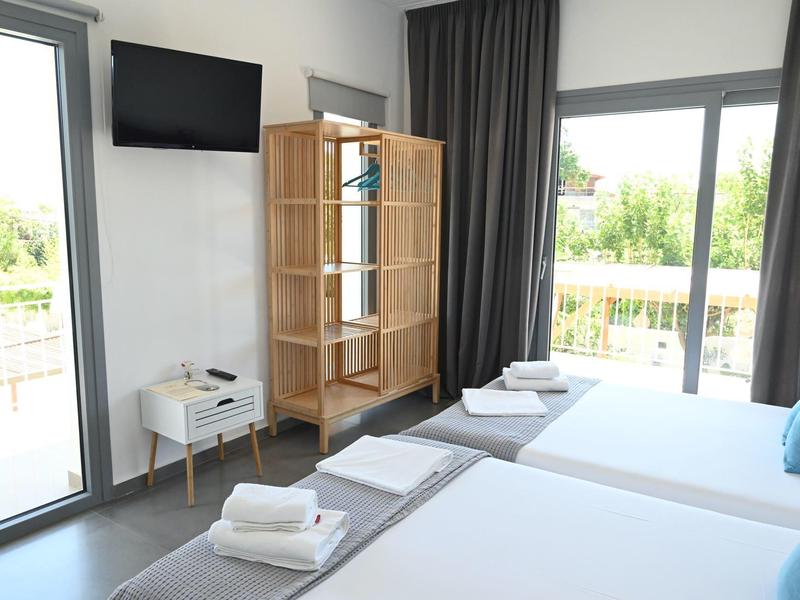 Habitación de hotel moderna con dos camas, vista al balcón y televisor en la pared.