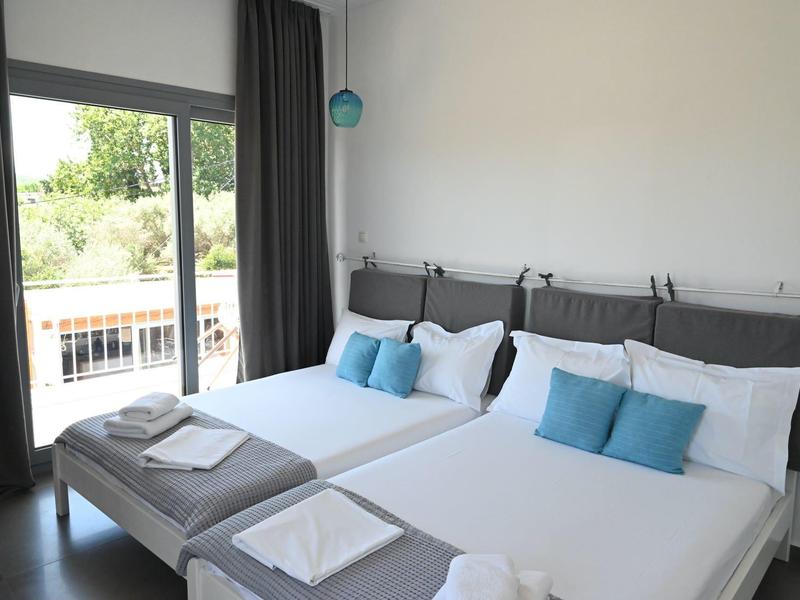 Habitación de hotel moderna con dos camas, ropa blanca y balcón con vista a la vegetación.