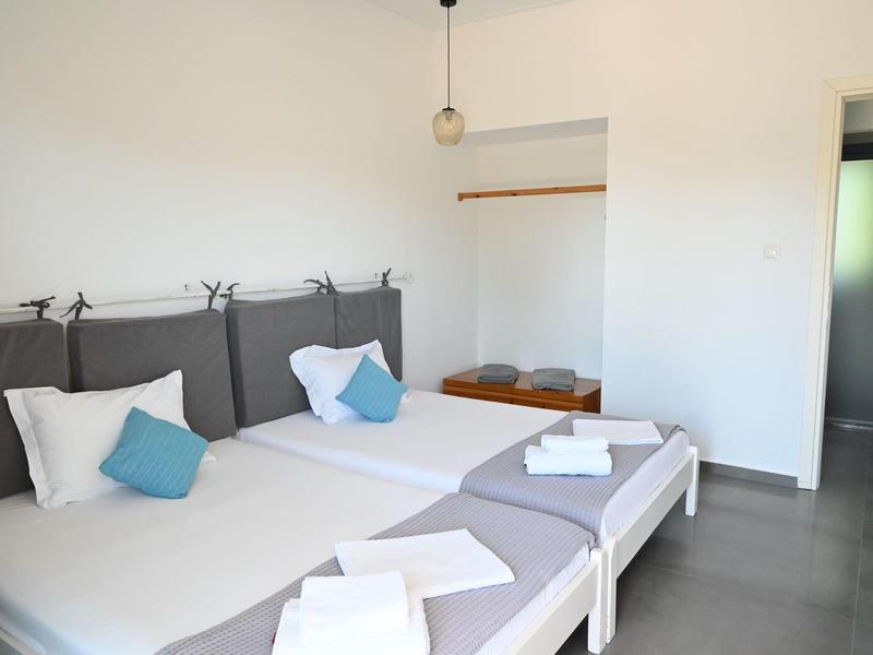 Habitación de hotel sencilla con dos camas individuales, almohadas blancas y azules, paredes blancas y armario abierto.