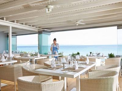 Elegancka restauracja z widokiem na morze i nakrytymi stołami w jasnym wnętrzu.