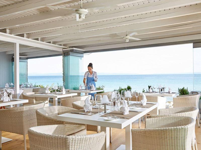 Elegancka restauracja z widokiem na morze i nakrytymi stołami w jasnym wnętrzu.