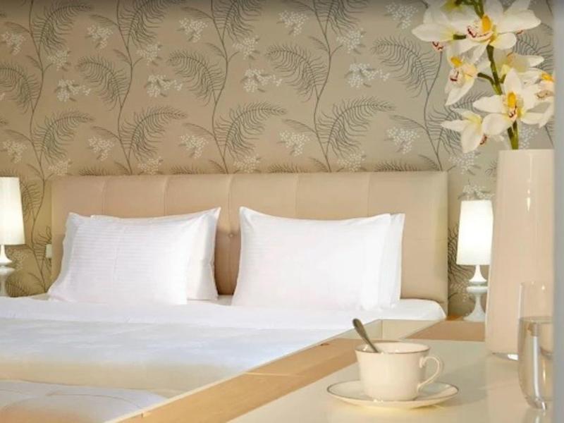 Jasno urządzony pokój hotelowy z łóżkiem podwójnym, lampkami nocnymi i dekoracyjną tapetą