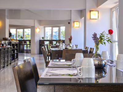 Elegantes Restaurant mit gedeckten Tischen und Stühlen, hellem Licht und Blumendekoration.