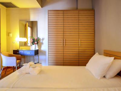 Camera d'hotel luminosa con letto grande, armadio in legno, tavolo trucco con sedia e fiori.