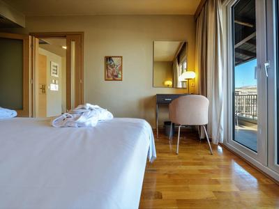 Camera d'hotel con letto, scrivania, sedia e balcone con vista sulla città.