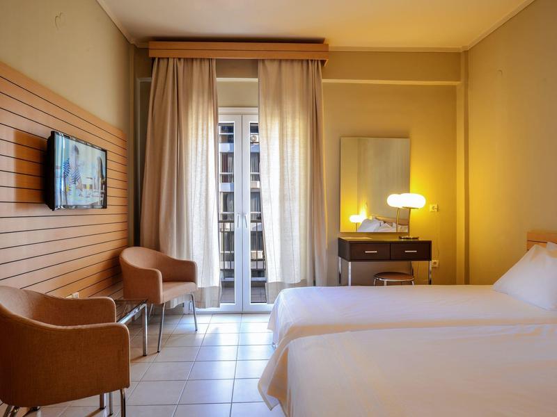 Camera d'hotel con due letti, due sedie, comò con lampada e vista sul balcone.