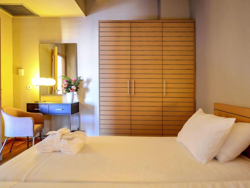 Camera d'hotel luminosa con letto grande, armadio in legno, tavolo trucco con sedia e fiori.