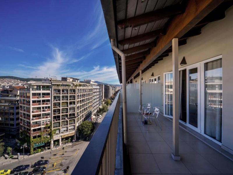 Balcone con sedie e tavoli in un hotel con vista sulla città e cielo azzurro.