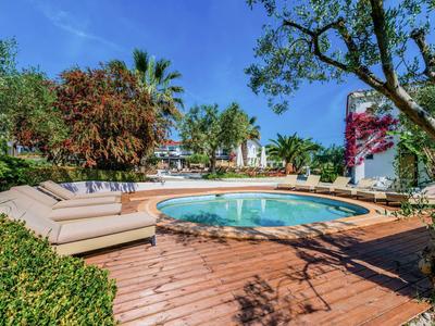 Piscina rotonda su terrazza in legno con lettini, palme e alberi sullo sfondo.