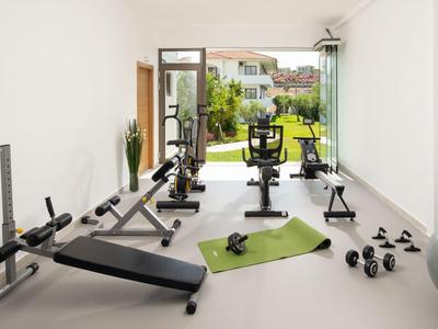 Bright gym room with fitness equipment and view of garden and building.