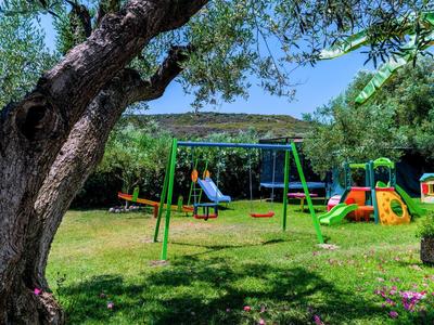 Area giochi con altalene, scivoli e attrezzature per arrampicata in un giardino verde sotto un cielo azzurro limpido.