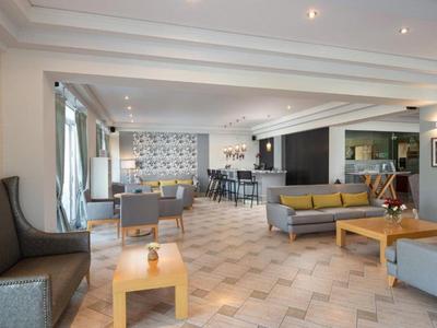 Lounge d'hotel moderna con divani, poltrone, tavoli e ampia zona luminosa.