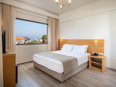 Camera d'hotel luminosa con letto matrimoniale, comodino e finestra con vista su edifici.