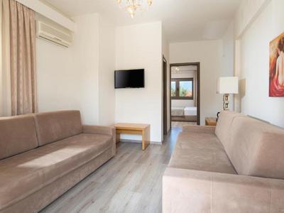 Soggiorno luminoso con due divani beige, TV a muro, pavimento in laminato e finestra con tende.