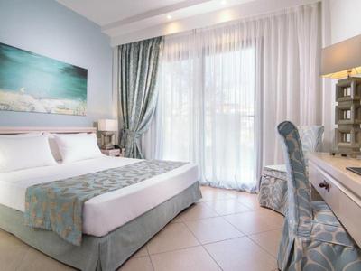 Camera d'hotel luminosa con letto matrimoniale, scrivania, sedia e grande finestra con tende.