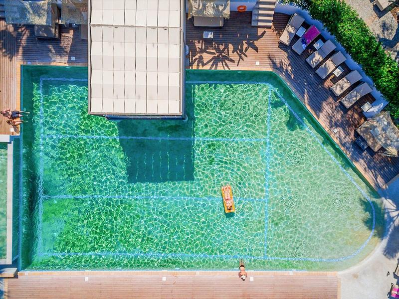 Vista aerea di una piscina rettangolare con lettini e ombrelloni lungo il bordo.
