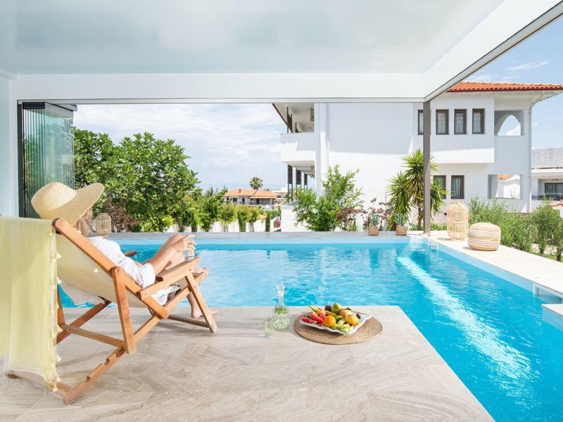 Donna che si rilassa su una sdraio accanto a una piscina con edifici e cielo sullo sfondo.