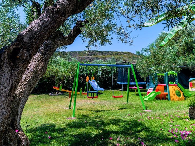 Area giochi con altalene, scivoli e attrezzature per arrampicata in un giardino verde sotto un cielo azzurro limpido.