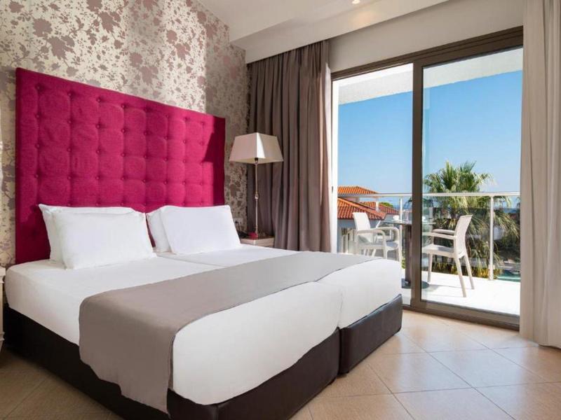 Camera d'hotel moderna con due letti singoli, testiera rosa e balcone con vista mare.