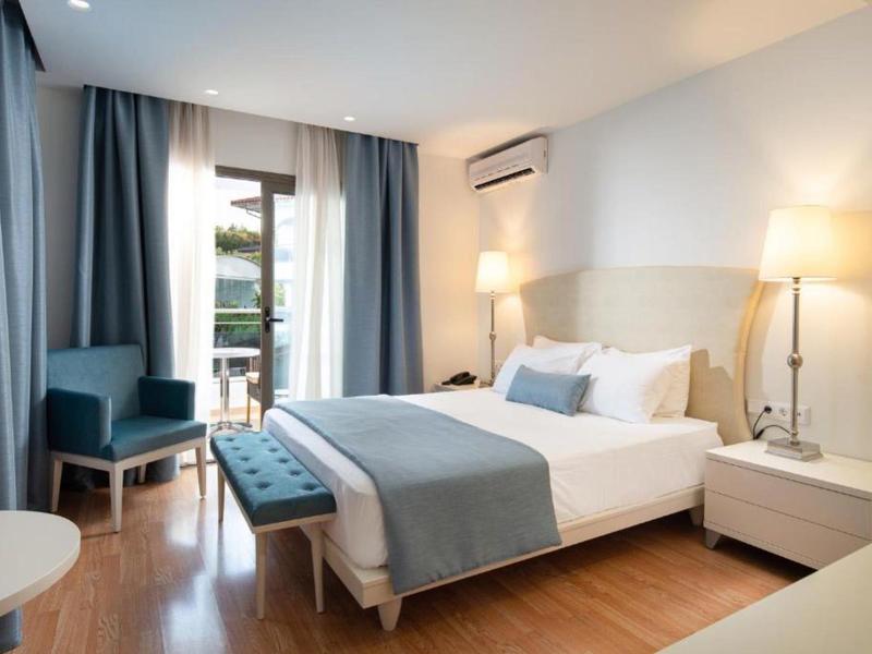 Camera d'hotel moderna con letto matrimoniale, zona salotto e accesso al balcone con luce naturale.