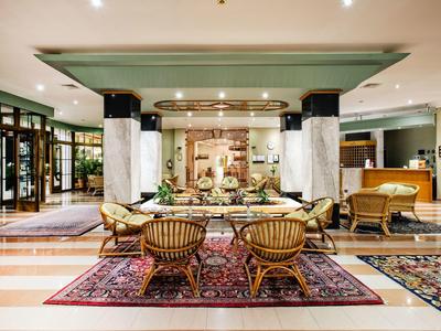 Elegancka lobby hotelowa z fotelami, dywanami i centralną dekoracją na długim stole.