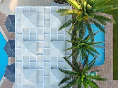 Widok z drona na nowoczesny hotel z basenem i palmami na jasnym tle.