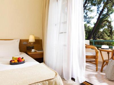 Jasny pokój hotelowy z łóżkiem, miską owoców i dostępem do balkonu z krzesłami.