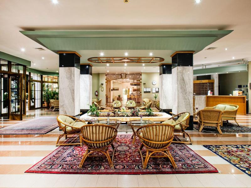 Elegancka lobby hotelowa z fotelami, dywanami i centralną dekoracją na długim stole.