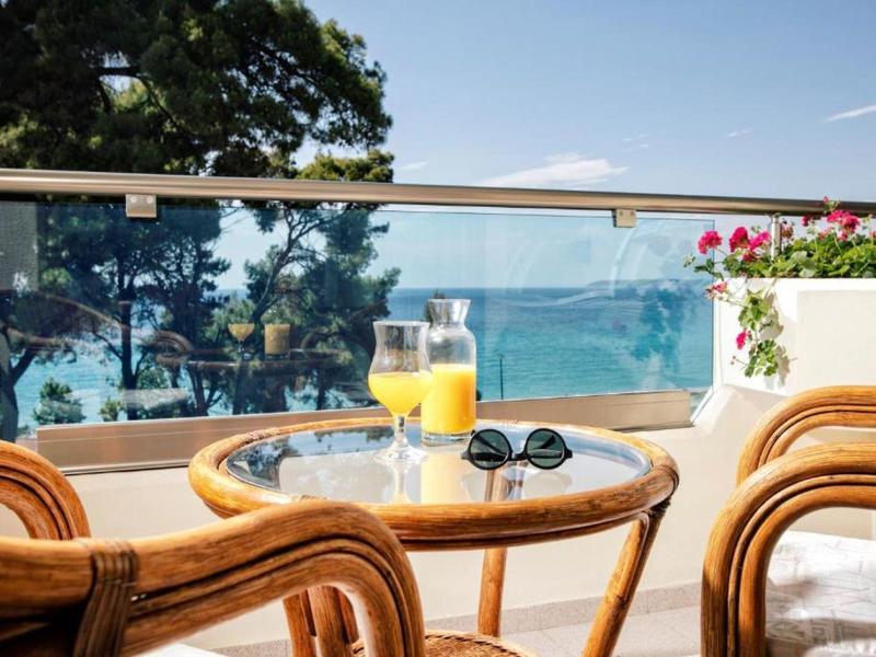 Balkon z stołem, krzesłami, szklanką soku, okularami przeciwsłonecznymi i widokiem na morze.