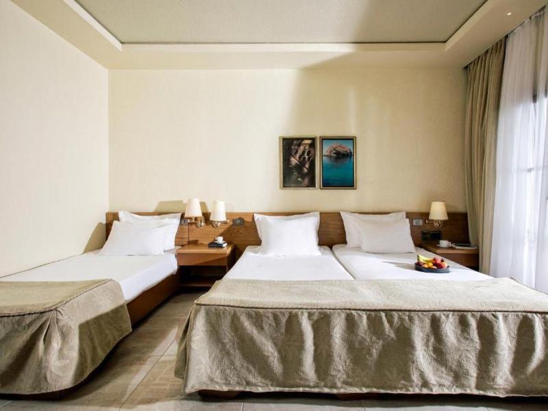 Jasny pokój hotelowy z dwoma łóżkami, stolikami nocnymi i dużymi oknami z zasłonami.