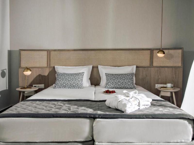 Nowoczesny pokój hotelowy z dwoma pojedynczymi łóżkami, beżową ścianą zagłówka i stylowymi lampkami nocnymi.