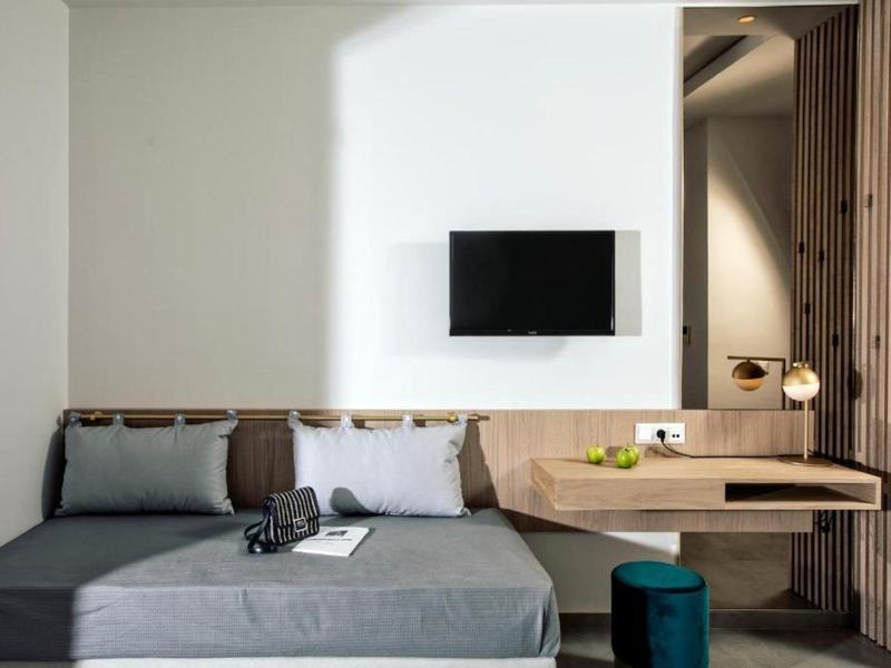 Nowoczesna część pokoju hotelowego z szarą sofą, drewnianą półką, telewizorem i minimalistycznym designem.