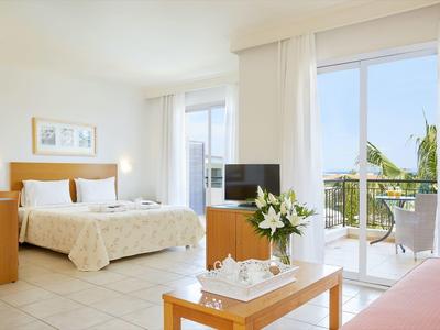 Jasny pokój hotelowy z podwójnym łóżkiem, drewnianymi meblami i balkonem z widokiem na morze.