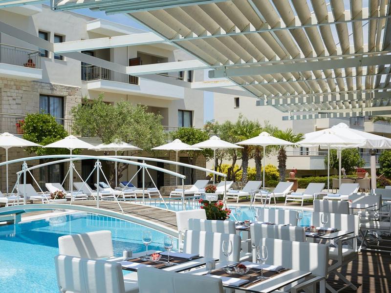 Nowoczesny zewnętrzny basen z biał-beżowymi parasolami i wygodnymi miejscami do siedzenia w hotelu.