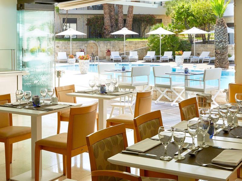 Widok na restaurację z nakrytymi stołami i strefą basenową z parasolami w tle.