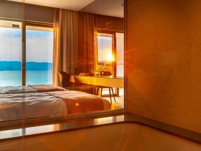 Modern hotel room with large windows and ocean view at sunset.