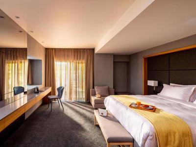 Modern hotel room with large bed, desk, and balcony with curtains.