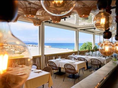 Cozy restaurant with sea view, white tables, and warm lighting