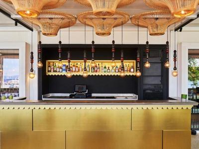 Modern hotel bar area with stylish wooden ceiling lamps and large windows showing city views.