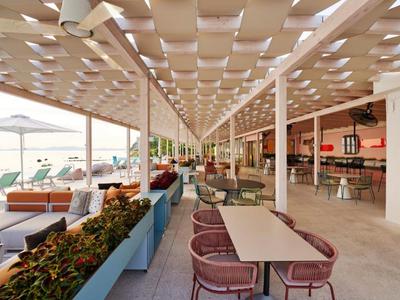 Modern hotel terrace with tables, chairs, umbrellas, and a view of the swimming pool.