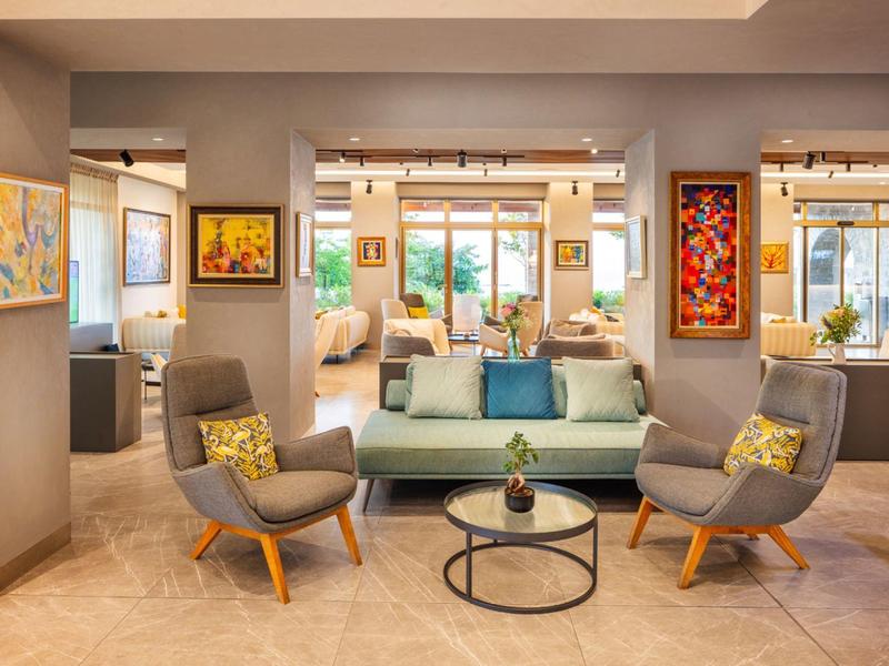 Modern living room with sofa, two chairs, and coffee table beneath large windows.